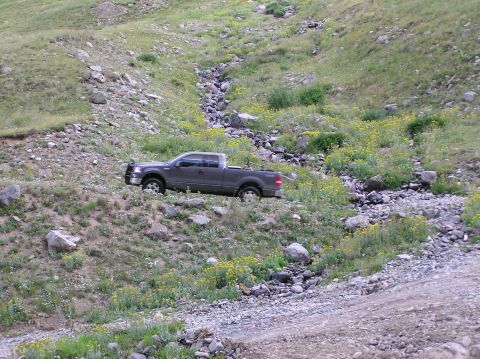 1986 Ford Bronco - Ford F-150 pickup truck navigates a challenging off-road terrain on a hillside.