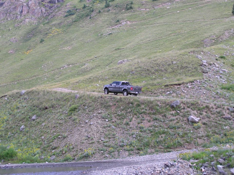 Gray Ford F-150 pickup truck on a dirt road in a grassy mountain area