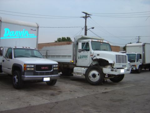 1992 Ford Bronco - Multiple trucks are parked on a lot, including a GMC pickup and a damaged dump truck.