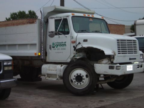 1992 Ford Bronco - A white dump truck with visible damage to its front end and a company logo on the door is parked next to another vehicle.