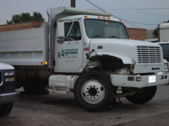 White dump truck with front-end damage and 'a touch of green' logo