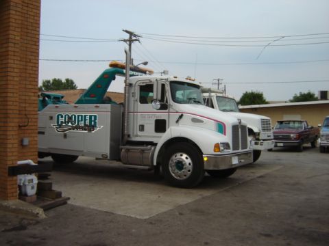 1992 Ford Bronco - A white tow truck with 'COOPER' branding is parked outside. Other vehicles are visible in the background.