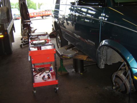 1992 Ford Bronco - A dark green van is undergoing service on a lift, with its front wheel removed and a red tool cart positioned beside it.