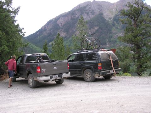 1986 Ford Bronco - Two vehicles, a pickup and an SUV, are parked on a dirt road with a mountain landscape behind them.