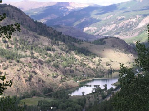 1986 Ford Bronco - A scenic view of a mountain valley a calm lake and lush green trees, with a watermark in the lower right corner.