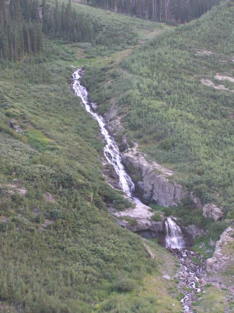 1986 Ford Bronco - A long waterfall flows down a green mountain slope with trees and rocks visible.