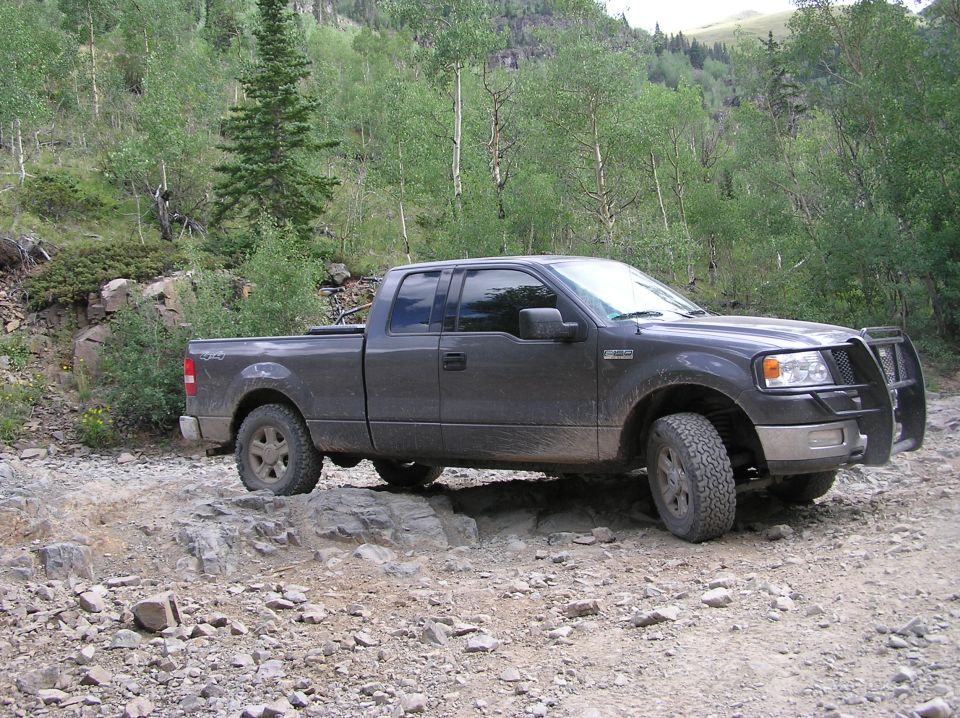 Dark gray Ford F-150 pickup truck with a bull bar, driving on a rocky mountain trail
