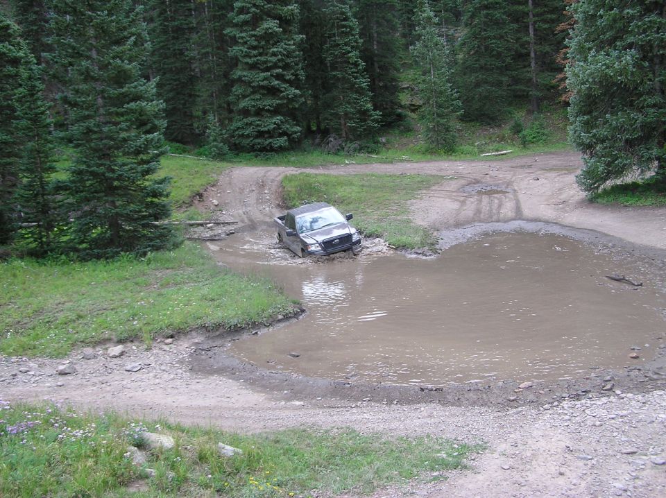 Dark gray Ford F-150 stuck in a muddy puddle on a dirt road