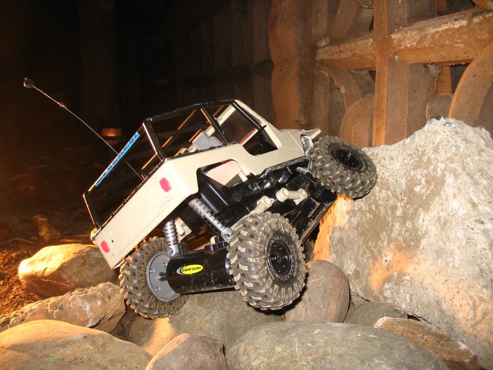 Tan RC crawler with black roof and roll cage perched on a boulder at a steep angle