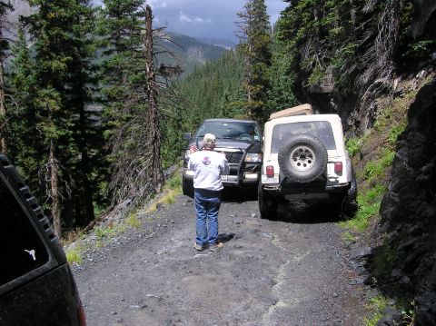 1986 Ford Bronco - A group of off-road vehicles navigate a steep, wooded mountain trail.