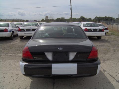 2000 Ford Crown Victoria - Several police vehicles are parked in an outdoor lot, with a black Crown Victoria in the foreground.