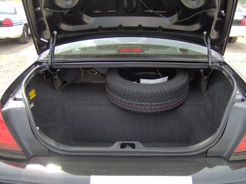 2000 Ford Crown Victoria - The trunk of a black Ford Crown Victoria is open, revealing a spare tire and carpeting, with another police car visible in the background.