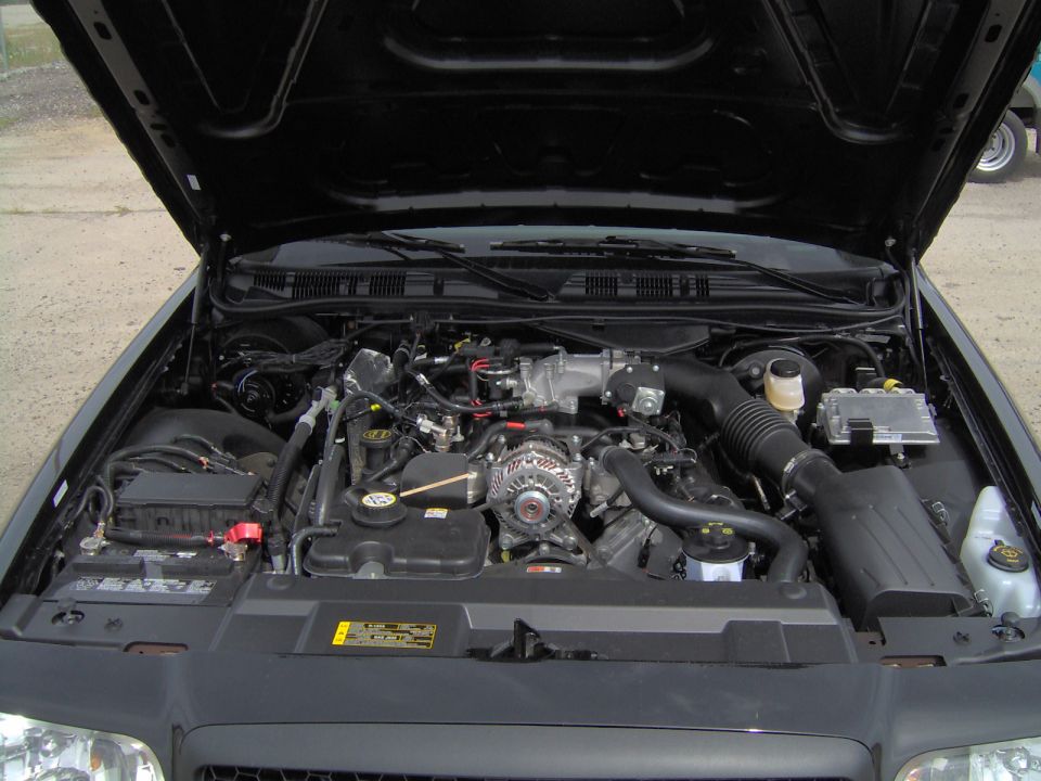 Open engine bay showing V8 engine, alternator, hoses and reservoir
