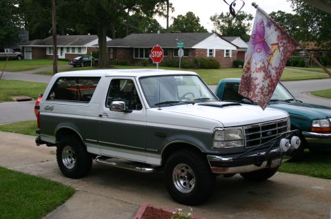 1994 Ford Bronco - A two-tone white and gray Ford Bronco is parked on a driveway next to a green pickup truck.