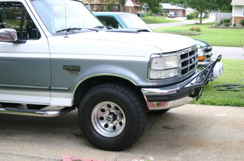 1994 Ford Bronco - Front three-quarter close-up of a white-over-gray two-tone Ford Bronco XLT parked on a driveway, showing the "BRONCO XLT 5.0" fender badge,…