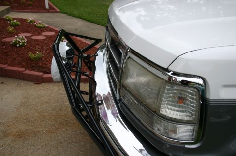 1994 Ford Bronco - Close-up of the passenger-side front corner of a white and gray two-tone Ford truck, showing the chrome bumper, composite headlight with cl…