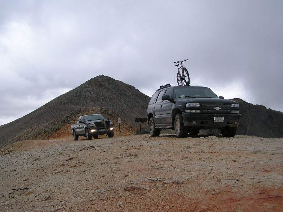 Black SUV with bicycle on roof, pickup truck in background on mountain road