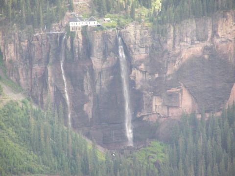 1986 Ford Bronco - Waterfall cascading down a cliff face with buildings on top, surrounded by trees.