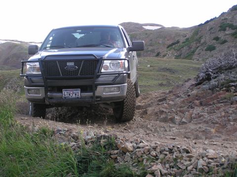 1986 Ford Bronco - This truck is navigating a rough, mountainous trail with sparse vegetation.