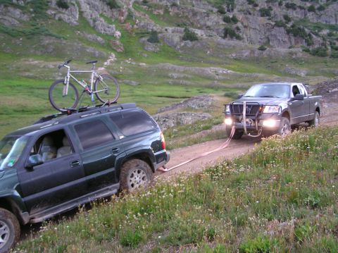1986 Ford Bronco - Two vehicles navigate a steep, grassy mountain road with a tow strap connecting them.