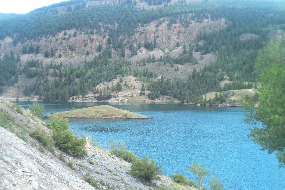 Water body with island and forested mountains in background. Supermotors.net logo in lower right