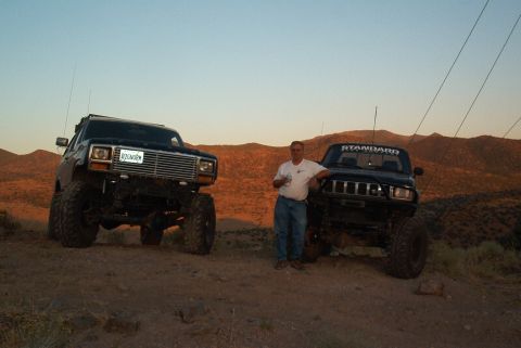 1986 Ford Bronco - Two off-road vehicles are parked on a dusty incline with a man standing between them.