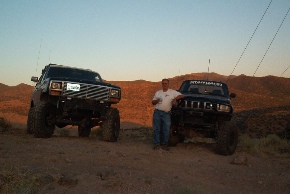 Man standing between two lifted trucks on a dirt hill