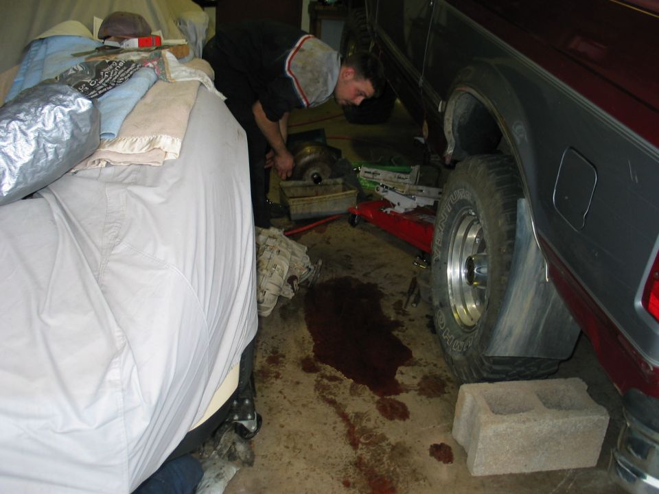 Maroon and grey SUV side view, mechanic working on transmission, fluid on floor