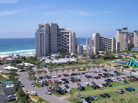 1995 Ford Bronco - A wide view of a parking lot filled with vehicles, situated near beachfront buildings under a clear blue sky.