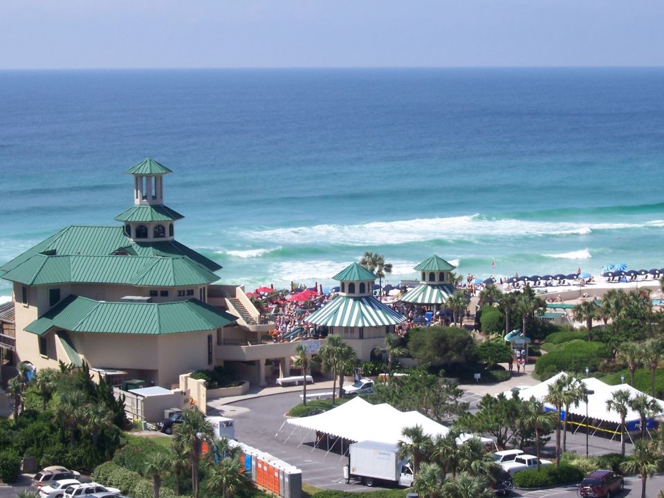 Beach resort with green roofs and ocean in background. Some tents and parked cars visible