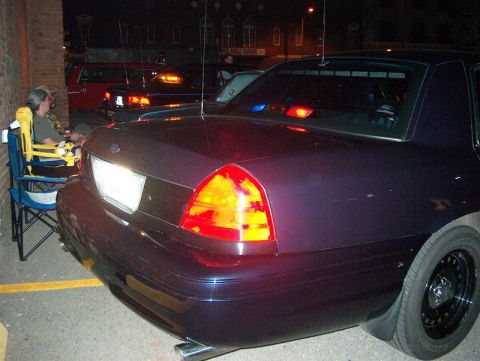 2001 Ford Crown Victoria - A dark purple 2001 Ford Crown Victoria Police Interceptor is parked at night, showing its rear end and police lights.