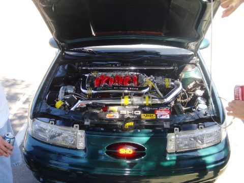 1991 Ford Taurus - The engine bay of a 1991 Ford Taurus SHO is displayed with its hood open, highlighting the V8 engine and custom parts.