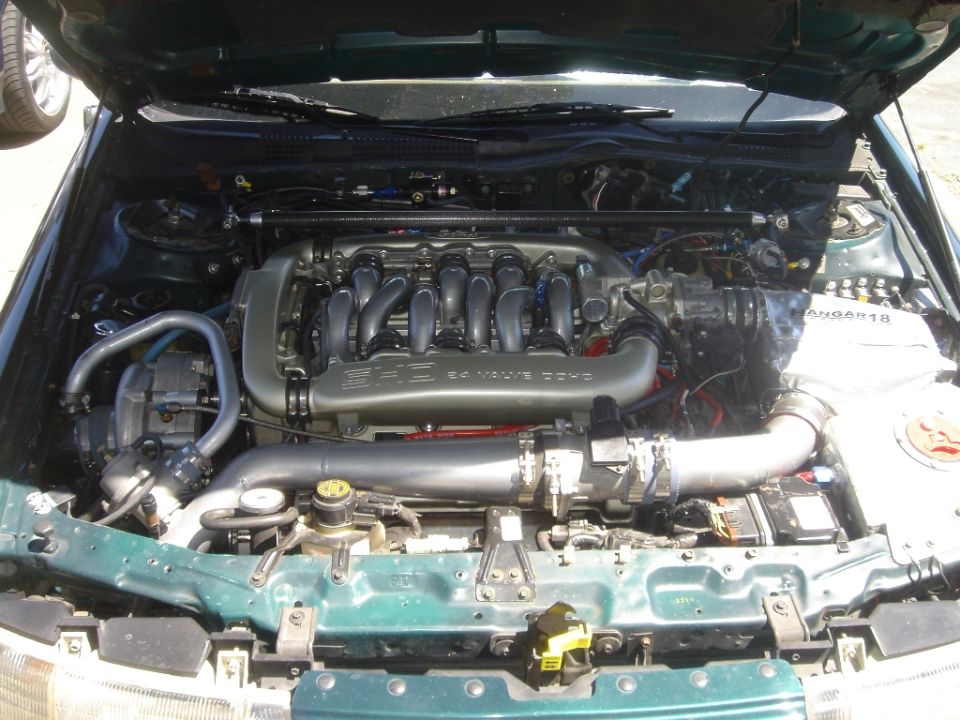 Green engine bay with a V6 engine, silver intake manifold, and turbocharger. Visible text 'SUPER MOTORS'