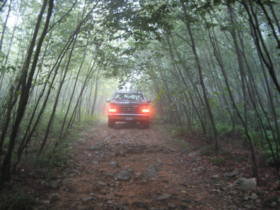 Dark Ford truck with brake lights lit climbing a rocky wooded trail in misty forest