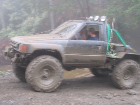 1992 Ford Bronco - This heavily modified Toyota pickup truck is navigating a muddy off-road trail with two people inside.