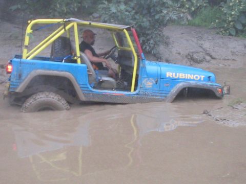 1992 Ford Bronco - A blue Jeep Wrangler with a yellow roll cage is stuck deep in the mud.
