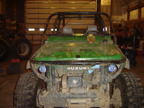 1992 Ford Bronco - A green Suzuki Samurai sits in a garage, equipped with a roll cage and winch, ready for off-road adventures.