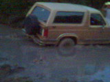 1983 Ford Bronco - A tan Ford Bronco from the 1980s is stuck in the mud, with its rear visible.