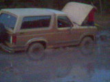 1983 Ford Bronco - This 1983 Ford Bronco appears to be stuck in the mud, with its hood propped open, suggesting a mechanical issue or a need for assistance.
