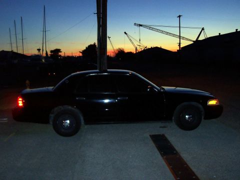 2003 Ford Crown Victoria - A black 2003 Ford Crown Victoria is parked outdoors during twilight, with a harbor and industrial cranes in the background.