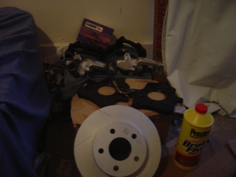 1998 Ford Taurus - A collection of brake components, including a rotor, calipers, and a bottle of brake fluid, are laid out.