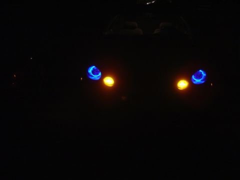 1998 Ford Taurus - The front of a car is visible at night, showing its illuminated headlights with blue halo rings.