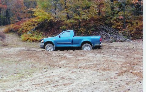 2001 Ford F-150 - A blue 2001 Ford F-150 pickup truck is stuck in a muddy, off-road environment.