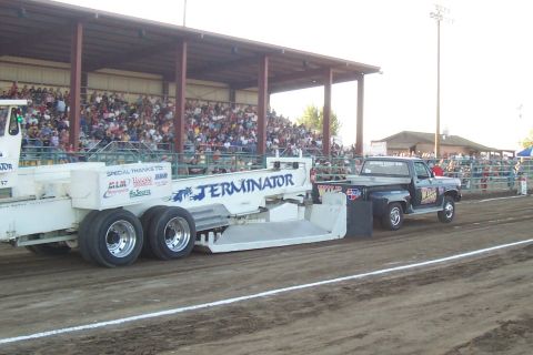 1994 Ford F-150 - A black pickup truck tows a "TERMINATOR" branded trailer during a pull event with spectators in the background.