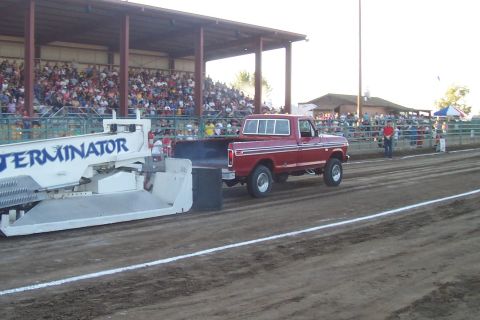 1994 Ford F-150 - A red pickup truck competes in a pull event, dragging a weighted sled in front of a crowd.
