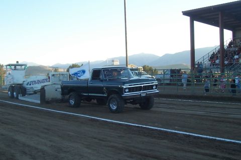 1994 Ford F-150 - A black Ford pickup truck, likely from 1975, competes in a pull event with a trailer and a Ford flag.