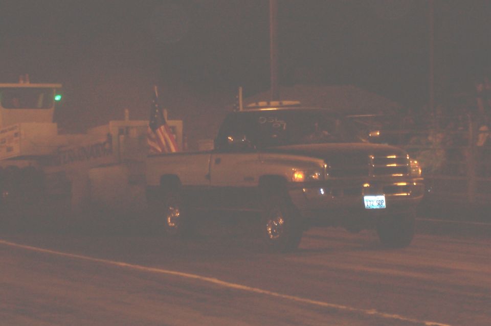 Pickup truck with American flag in bed, seen at night. License plate is visible
