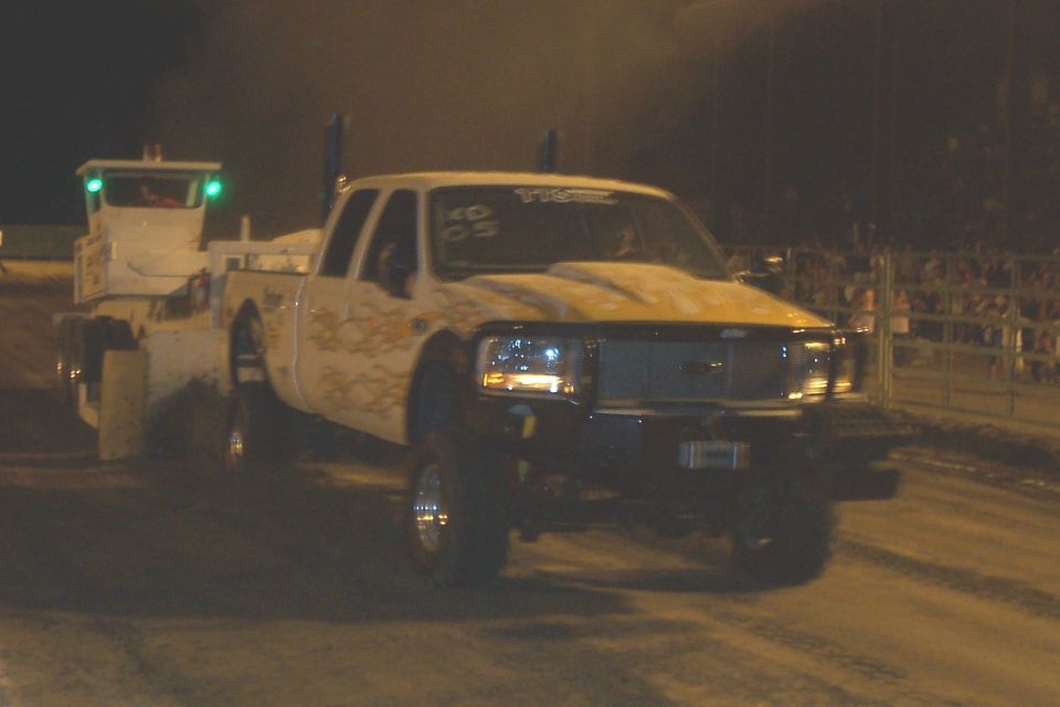 White pickup truck with flames and a tow truck at night. Text on windshield reads '05'