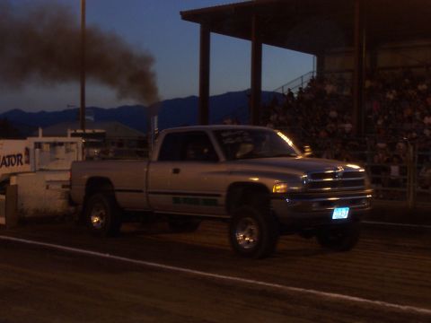 1994 Ford F-150 - A silver pickup truck pulls a trailer, emitting a large plume of dark smoke during a nighttime event.