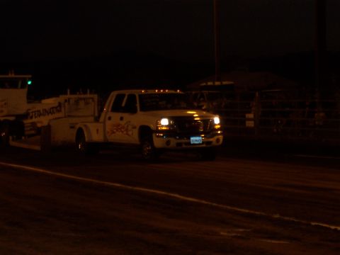 1994 Ford F-150 - A white pickup truck with decals tows a trailer in the dark, with headlights illuminated.